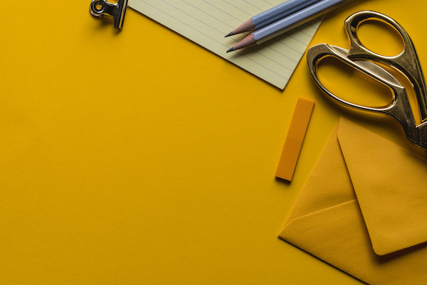 Image of yellow background, yellow envelope, scissors, pencils and paper