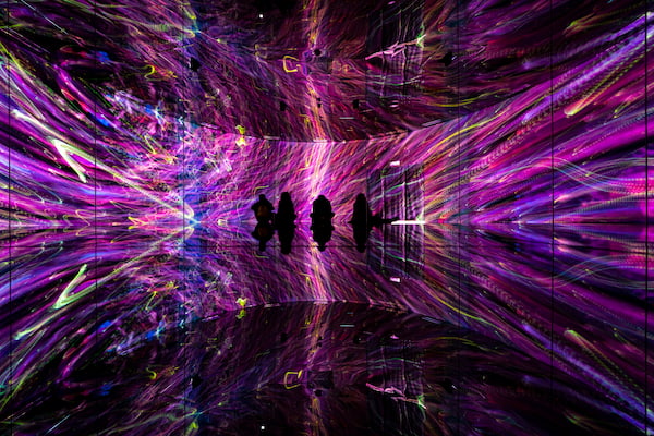 A dark, mysterious pink and purple space with people standing inside. In China, Shanghai, taken on November 22, 2019: Immersive Experience Exhibition Room at Epson